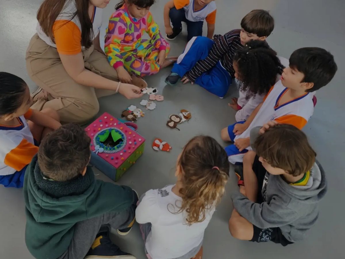 Crianças e professora sentadas no chão em atividade com jogos e brinquedos