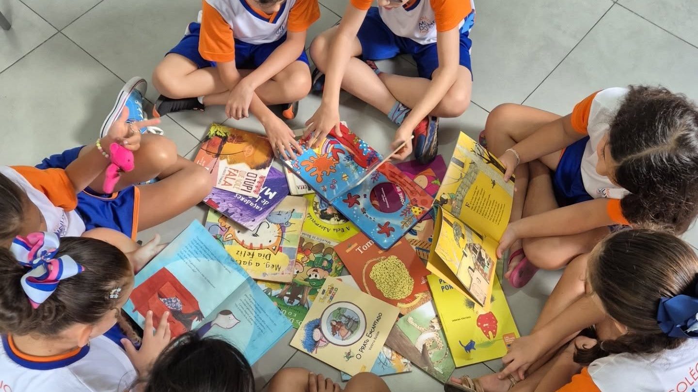 Crianças sentadas em roda no chão da sala, folheando livros ilustrados