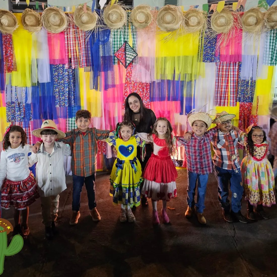 Crianças vestidas de caipira na Festa Julina, diante do painel colorido